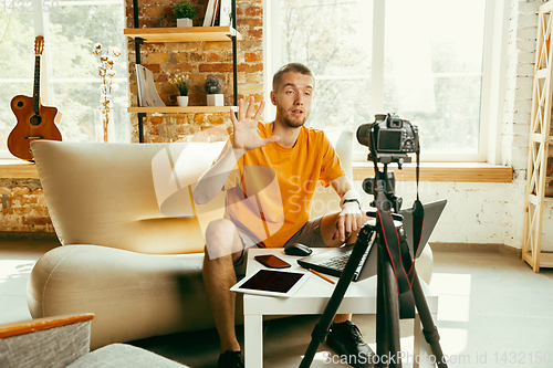 Image of Caucasian male blogger with camera recording video review of gadgets at home