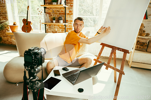 Image of Caucasian male blogger with camera recording video review of gadgets at home