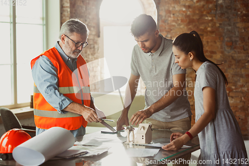 Image of Foreman or achitect shows house, office or store design plans to a young couple