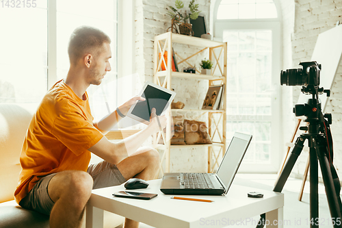 Image of Caucasian male blogger with camera recording video review of gadgets at home