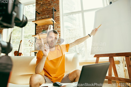 Image of Caucasian male blogger with camera recording video review of gadgets at home