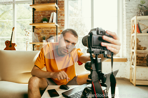 Image of Caucasian male blogger with camera recording video review of gadgets at home