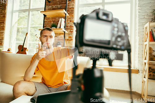 Image of Caucasian male blogger with camera recording video review of gadgets at home