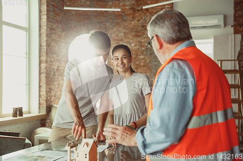 Image of Foreman or achitect shows house, office or store design plans to a young couple