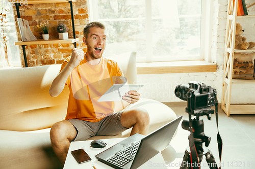 Image of Caucasian male blogger with camera recording video review of gadgets at home