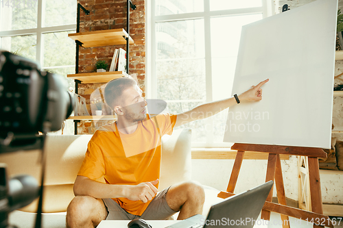 Image of Caucasian male blogger with camera recording video review of gadgets at home