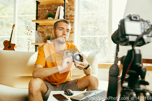 Image of Caucasian male blogger with camera recording video review of gadgets at home