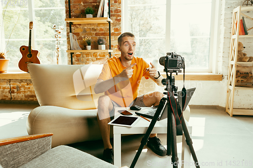 Image of Caucasian male blogger with camera recording video review of gadgets at home