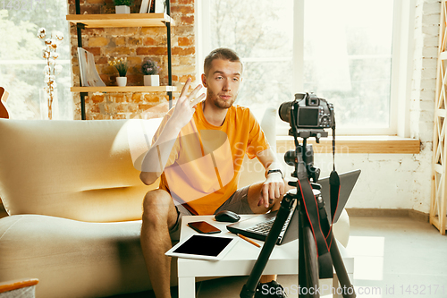 Image of Caucasian male blogger with camera recording video review of gadgets at home