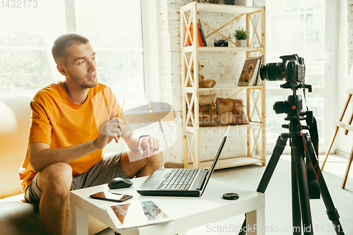 Image of Caucasian male blogger with camera recording video review of gadgets at home