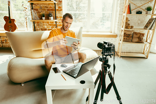 Image of Caucasian male blogger with camera recording video review of gadgets at home