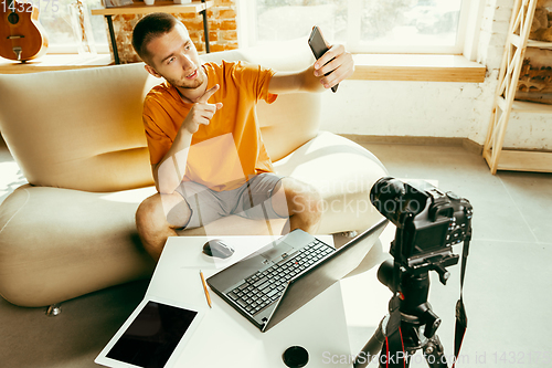 Image of Caucasian male blogger with camera recording video review of gadgets at home