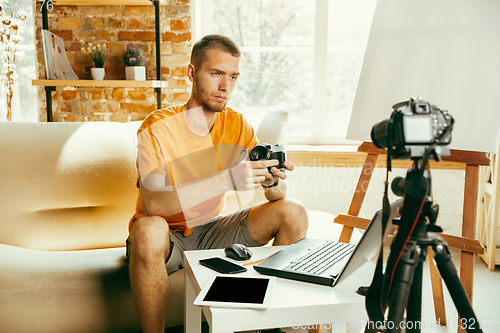 Image of Caucasian male blogger with camera recording video review of gadgets at home