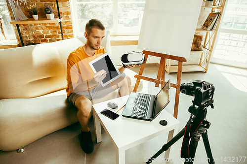 Image of Caucasian male blogger with camera recording video review of gadgets at home