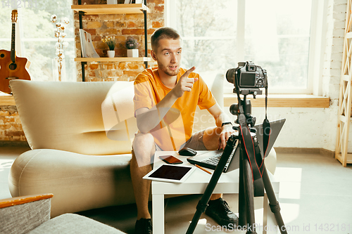 Image of Caucasian male blogger with camera recording video review of gadgets at home