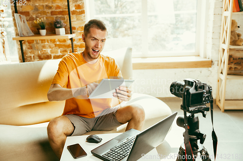 Image of Caucasian male blogger with camera recording video review of gadgets at home