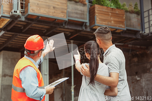 Image of Foreman or achitect shows house, office or store design plans to a young couple