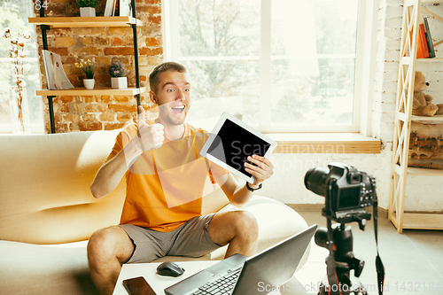 Image of Caucasian male blogger with camera recording video review of gadgets at home