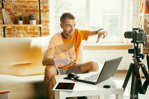 Image of Caucasian male blogger with camera recording video review of gadgets at home