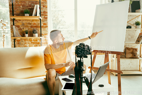 Image of Caucasian male blogger with camera recording video review of gadgets at home