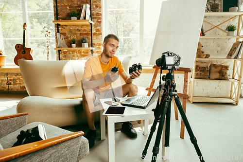 Image of Caucasian male blogger with camera recording video review of gadgets at home