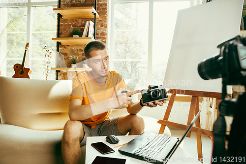 Image of Caucasian male blogger with camera recording video review of gadgets at home