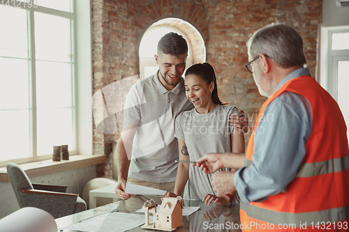 Image of Foreman or achitect shows house, office or store design plans to a young couple