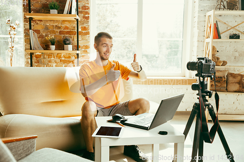 Image of Caucasian male blogger with camera recording video review of gadgets at home