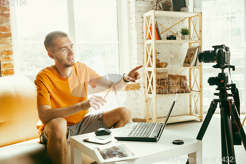 Image of Caucasian male blogger with camera recording video review of gadgets at home