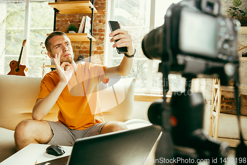 Image of Caucasian male blogger with camera recording video review of gadgets at home