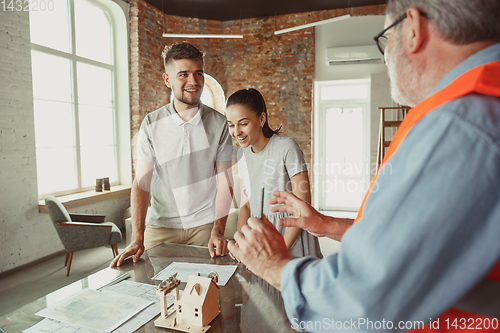 Image of Foreman or achitect shows house, office or store design plans to a young couple