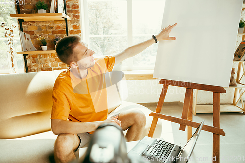 Image of Caucasian male blogger with camera recording video review of gadgets at home