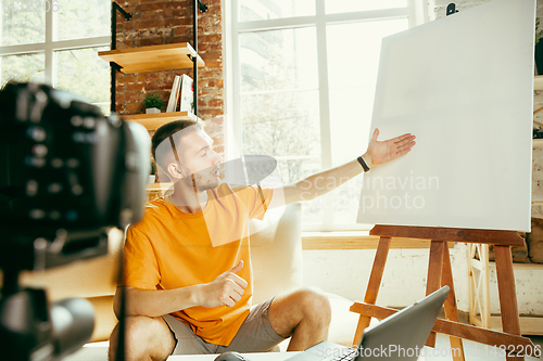 Image of Caucasian male blogger with camera recording video review of gadgets at home