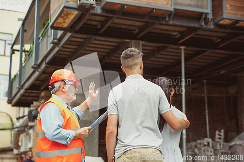 Image of Foreman or achitect shows house, office or store design plans to a young couple