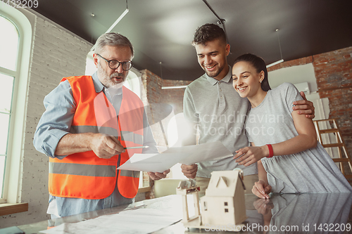 Image of Foreman or achitect shows house, office or store design plans to a young couple