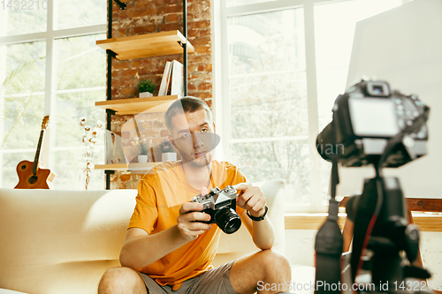 Image of Caucasian male blogger with camera recording video review of gadgets at home