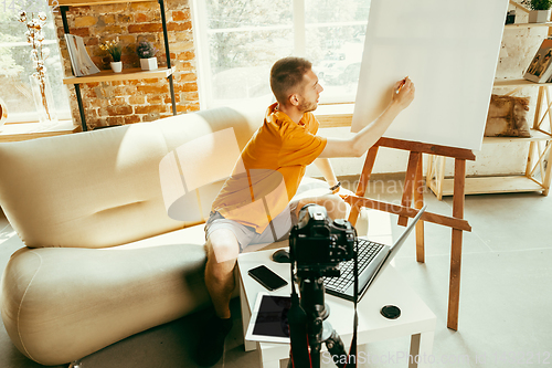 Image of Caucasian male blogger with camera recording video review of gadgets at home