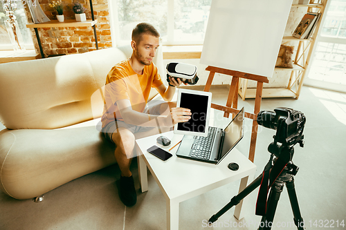 Image of Caucasian male blogger with camera recording video review of gadgets at home