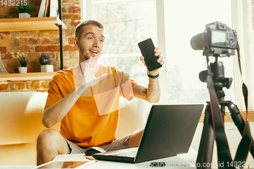 Image of Caucasian male blogger with camera recording video review of gadgets at home