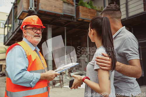 Image of Foreman or achitect shows house, office or store design plans to a young couple