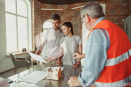 Image of Foreman or achitect shows house, office or store design plans to a young couple