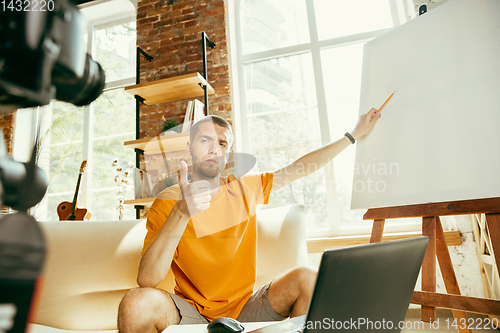 Image of Caucasian male blogger with camera recording video review of gadgets at home