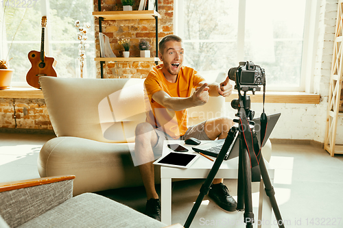 Image of Caucasian male blogger with camera recording video review of gadgets at home