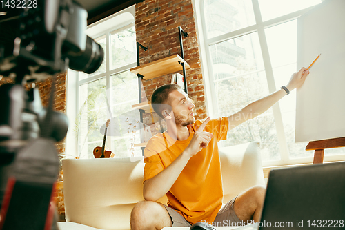 Image of Caucasian male blogger with camera recording video review of gadgets at home