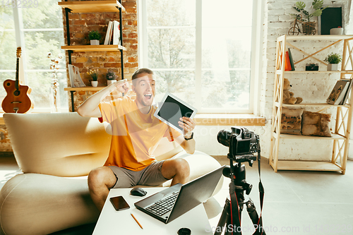 Image of Caucasian male blogger with camera recording video review of gadgets at home