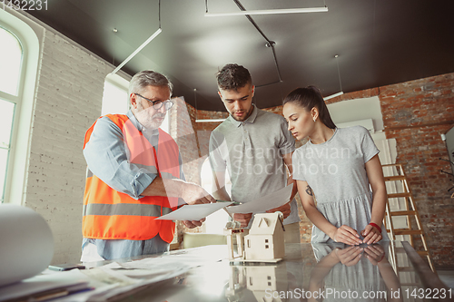 Image of Foreman or achitect shows house, office or store design plans to a young couple