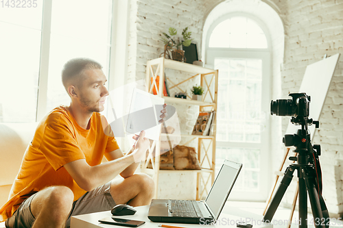 Image of Caucasian male blogger with camera recording video review of gadgets at home