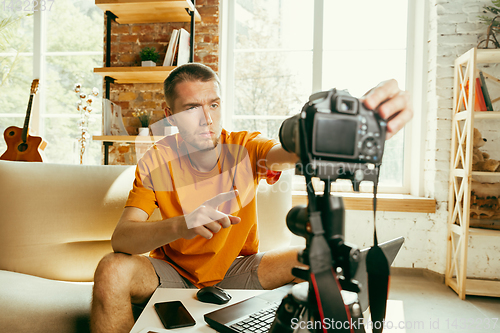 Image of Caucasian male blogger with camera recording video review of gadgets at home