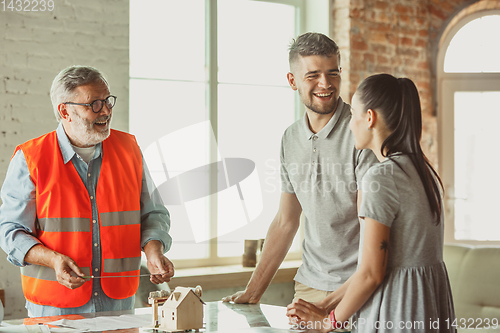 Image of Foreman or achitect shows house, office or store design plans to a young couple