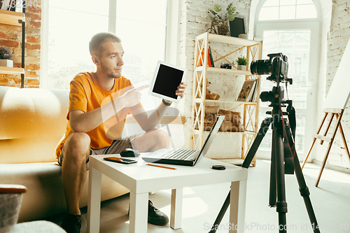 Image of Caucasian male blogger with camera recording video review of gadgets at home